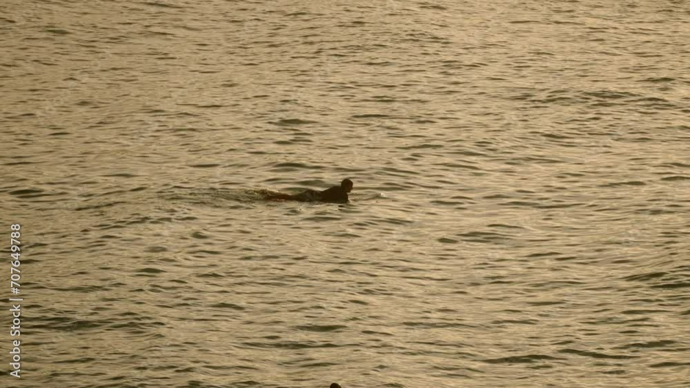 Surfer paddles out in golden sunset sea. Wave rider prepares for surf, adventure tourism. Ocean landscape, water sport in nature. Solo surfer seeks thrill, active lifestyle. Surfer paddles out in golden sunset sea. Wave rider prepares for surf, adventure tourism. Ocean landscape, water sport in nature. Solo surfer seeks thrill, active lifestyle.