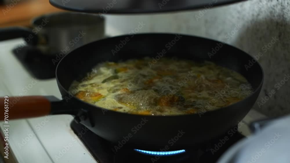 Lid open and close for pan of delicious pumpkin soup bubbling and boiling in frying pan, filmed as medium closeup shot in slow motion