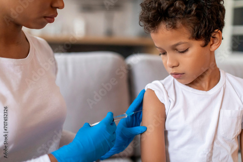 Doctor making vaccination against flu for little black boy in home interior photo