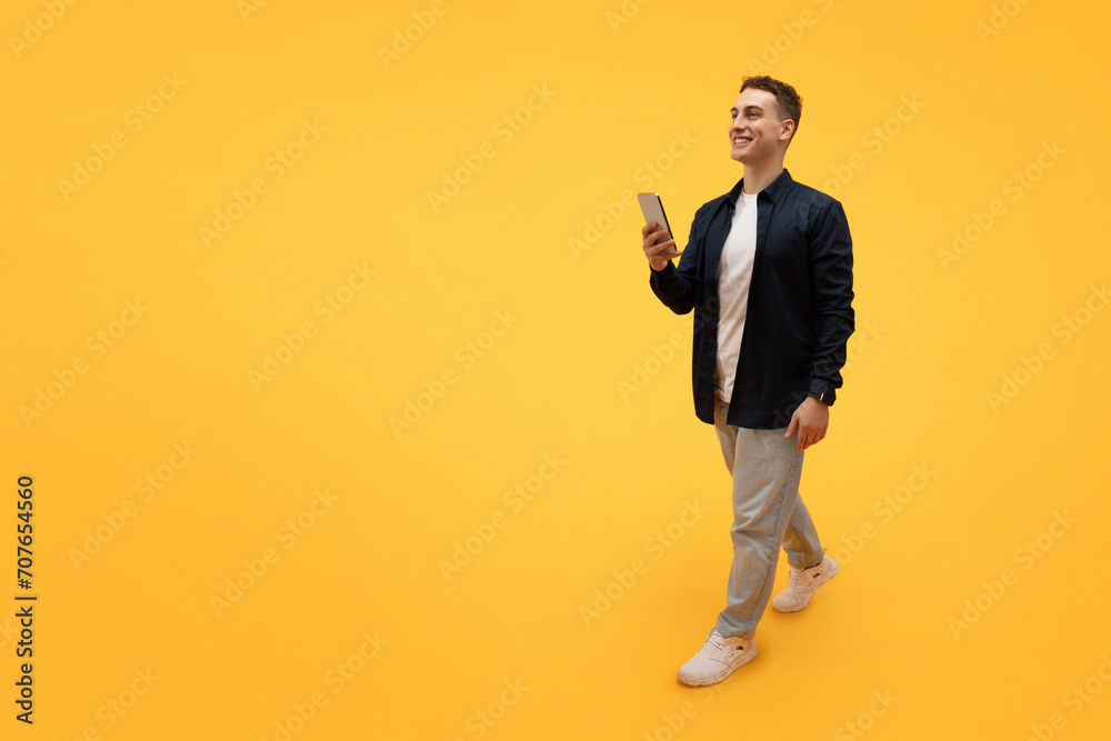 Stylish young guy using smartphone, texting friends, walking on yellow Stylish young guy using smartphone, texting friends, walking on yellow
