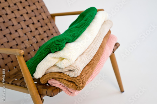 A stack of knitted clothes of different colors folded on a chair.