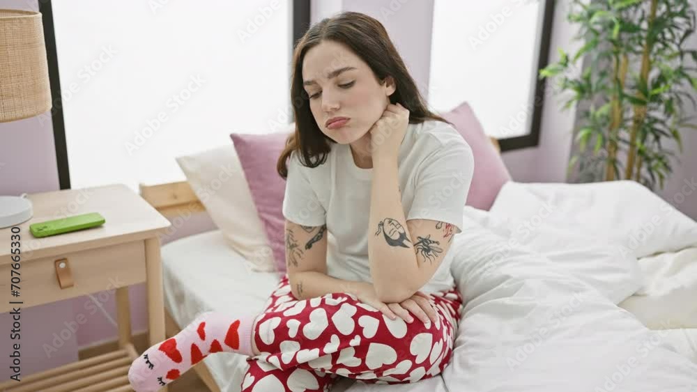 Young woman in pajamas sitting tired and bored on bed, depression crossing her thoughts in bedroom Young woman in pajamas sitting tired and bored on bed, depression crossing her thoughts in bedroom