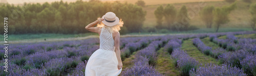 Beautiful young woman wearing a white dress walking in the middle of a lavender field in bloom