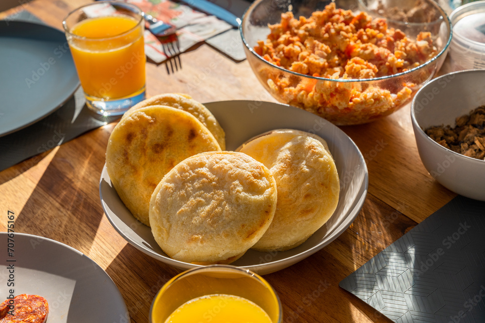 Arepas made of cornmeal in the center table next to scrambled eggs, meat and orange juice. Arepas made of cornmeal in the center table next to scrambled eggs, meat and orange juice.