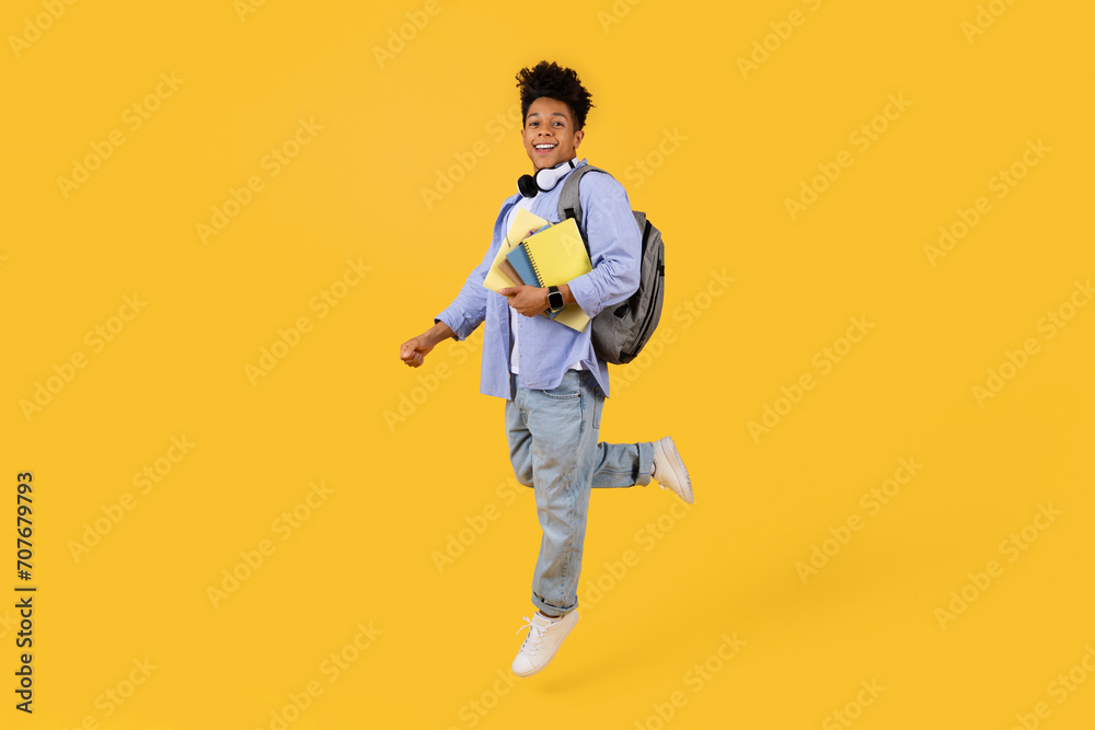 Joyful black male student running with books on vibrant yellow