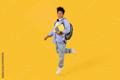 Joyful black male student running with books on vibrant yellow