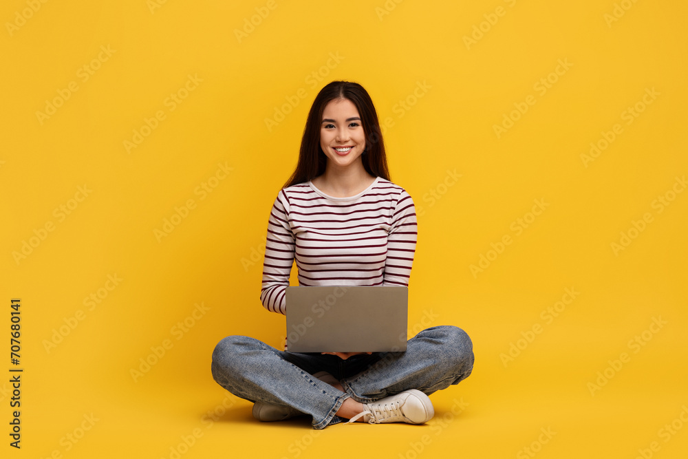 Positive young chinese lady student sitting on floor with laptop Positive young chinese lady student sitting on floor with laptop