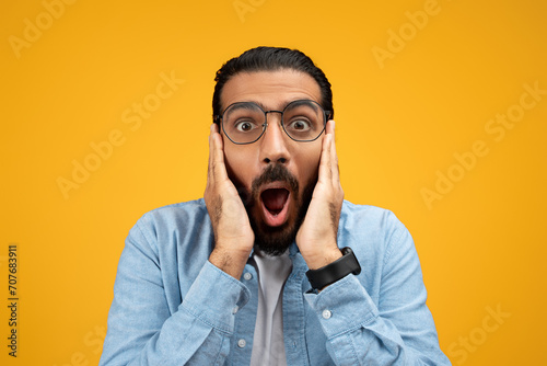 Shocked man in a blue shirt with hands on cheeks and mouth wide open © Prostock-studio