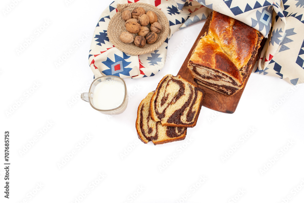 Fototapeta premium Cozonac, Romanian traditional sweet bread with walnut filling, sliced , with a glass of milk and patterned cloth, flat lay isolated