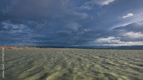 Fototapeta Naklejka Na Ścianę i Meble -  Surm am Bodensee, Wellen im Wasser, düstere Wolken. Sonne scheint wolkenlücke. Naturschutzgebiet im Hintergrund