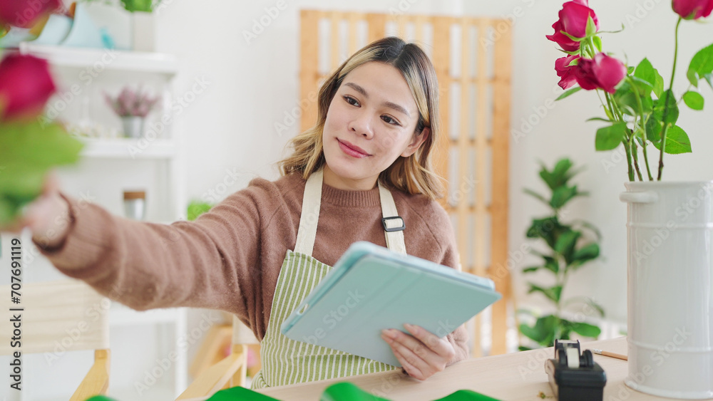 Small business concept. Young asian woman florist using tablet writing on order online at flower shop. Female florist or flower shop owner using tablet working, receiving order at flower shop Small business concept. Young asian woman florist using tablet writing on order online at flower shop. Female florist or flower shop owner using tablet working, receiving order at flower shop