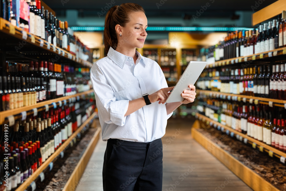 Businesswoman retail manager working on her digital tablet while standing in the wine shop sales area.