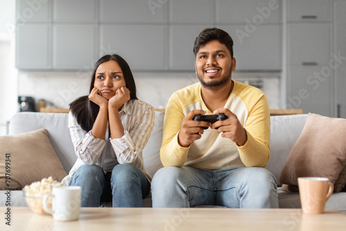 Bored young indian woman sitting near boyfriend playing video games at home