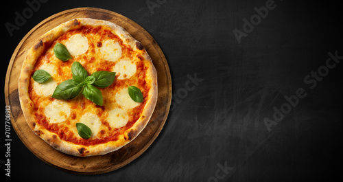Margherita pizza with mozzarella and tomato slices and basil green leaves, on an old wooden cutting board, against an empty blackboard with copy space. Generative Ai.