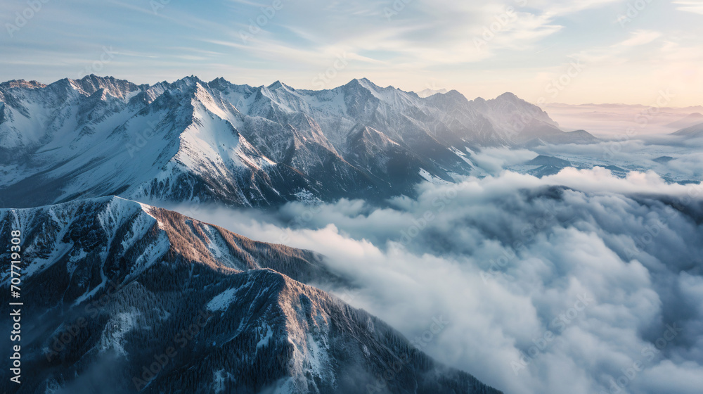 Aerial view of a serene mountain range in the early morning with snow-capped peaks and mist rolling through the valleys.