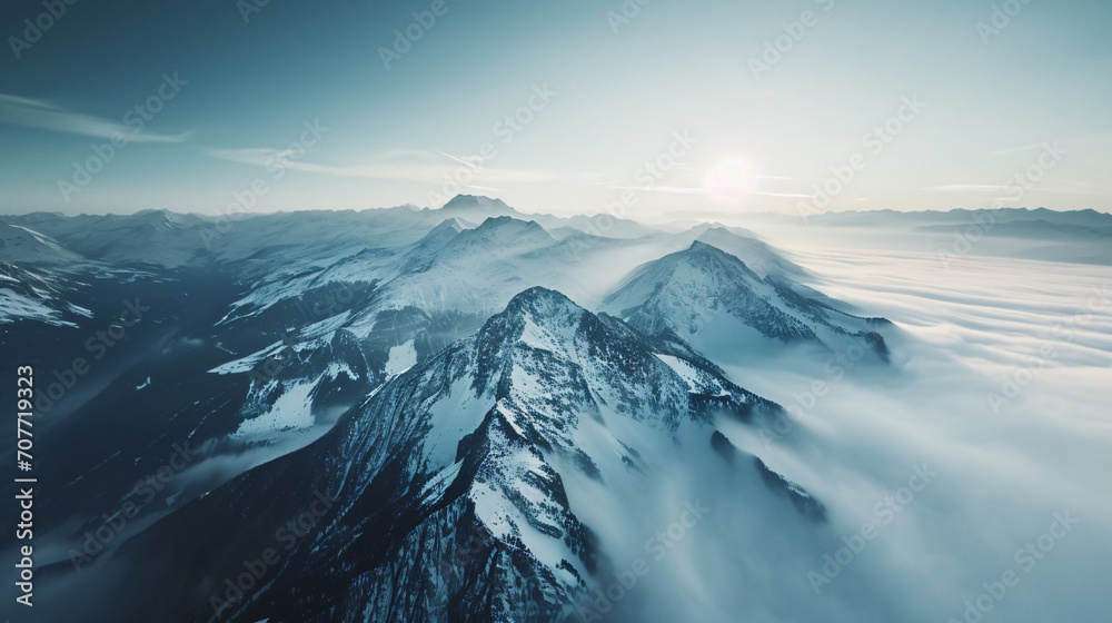 Aerial view of a serene mountain range in the early morning with snow-capped peaks and mist rolling through the valleys.