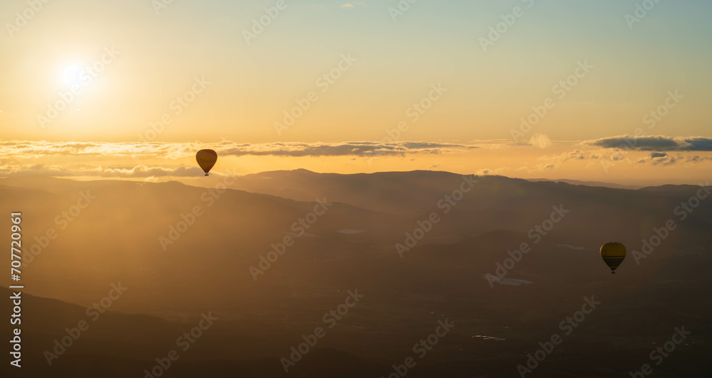 Vibrant scene of hot air balloons gliding over majestic mountain peaks at sunrise