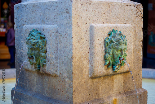 fountain with water in European city center with statues and faces