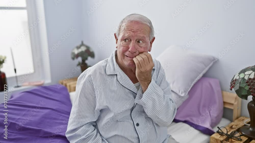 Stressed senior man in pyjamas, sitting on bed in bedroom, hands anxiously biting nails, showing signs of nervous anxiety problem.