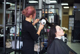 Professional hairdresser preparing to give a haircut to her beautiful cheerful female client combing her hai