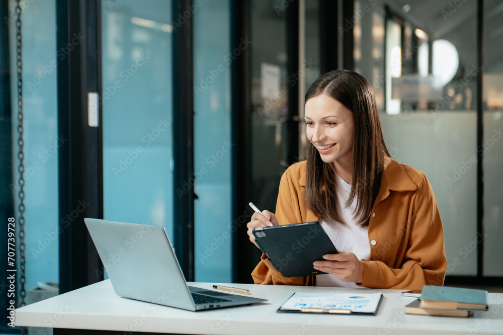 Business expert attractive smiling young woman typing laptop and holding digital tablet Business expert attractive smiling young woman typing laptop and holding digital tablet