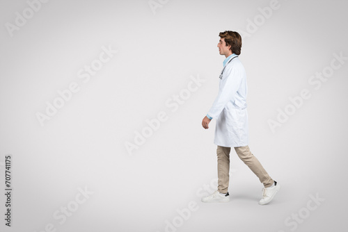 Walking male doctor in lab coat and casual attire, full length, free space