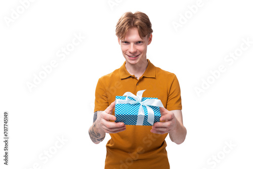 a young guy with short red hair dressed in a summer t-shirt holds a blue gift box in his hand for the holiday