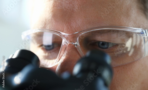 Handsome man scientist looking through binocular microscope examining diseases of the virus that infects water vivo ivf photo
