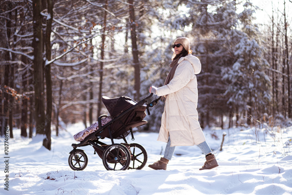 Mom and baby in a stroller on a walk in the winter forest.