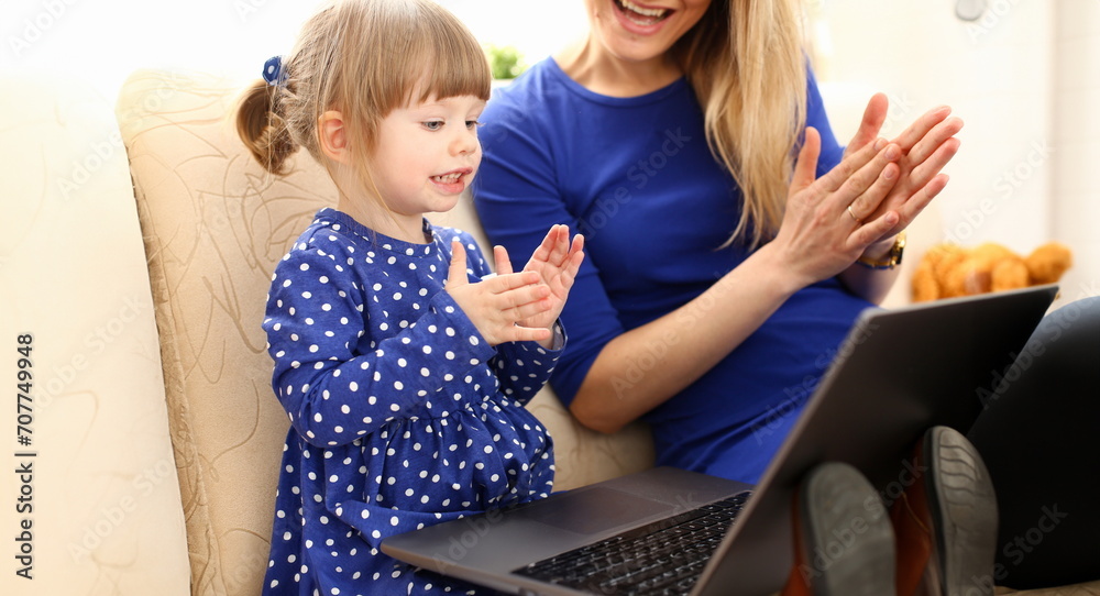 Cute little girl on couch with mom use laptop pc for chat with her dad away on business portrait. Point finger hand in display social web network bank mortgage credit wireless ip telephony concept - obrazy, fototapety, plakaty 