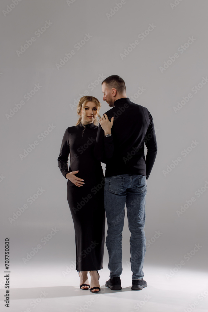 Photo of optimistic pregnant couple hugging, wearing dark clothes, sneakers, isolated on white background Photo of optimistic pregnant couple hugging, wearing dark clothes, sneakers, isolated on white background