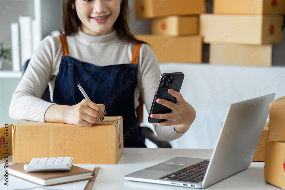 Young business entrepreneur using mobile and laptop. Preparing for shipping, online selling, e-commerce concept Young business entrepreneur using mobile and laptop. Preparing for shipping, online selling, e-commerce concept