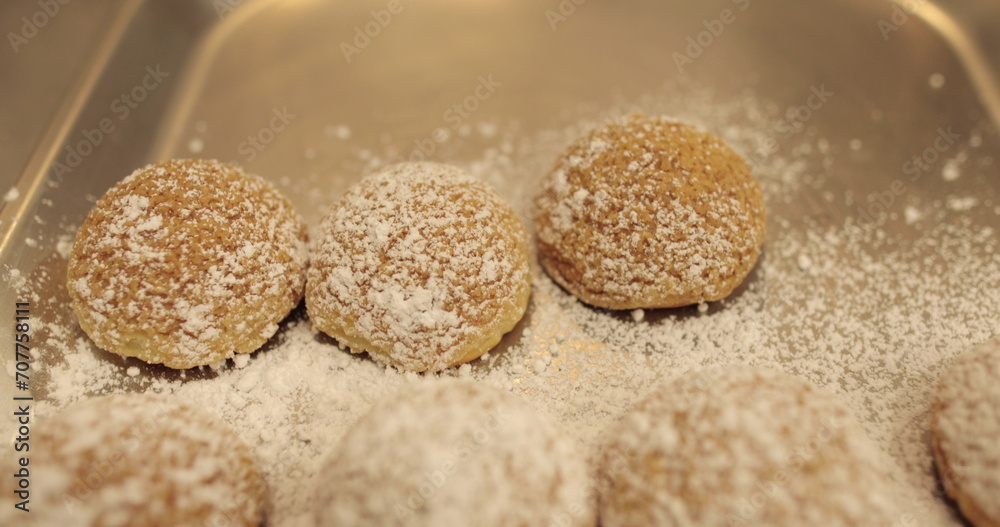 Ready-made cakes sprinkled with powdered sugar are stacked in even rows on a metal tray in a professional pastry shop.