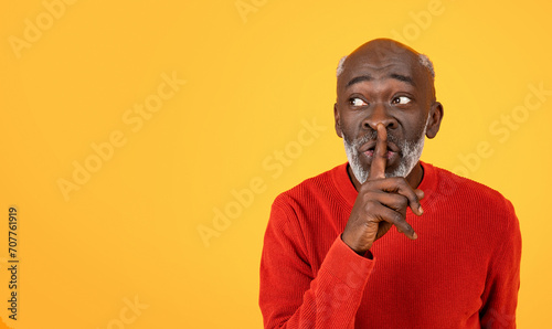 Secretive senior Black man with a white beard placing a finger to his lips in a shushing gesture