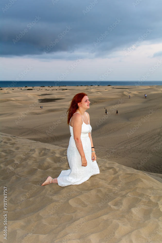 Young woman kneeling sadly in the sand dunes Young woman kneeling sadly in the sand dunes