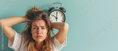 Creative concept of insomnia, sleep disorders, and problems waking up in the morning. A young woman with tousled hair, wide-eyed and puffed cheeks, facing an alarm clock, copy space. photo