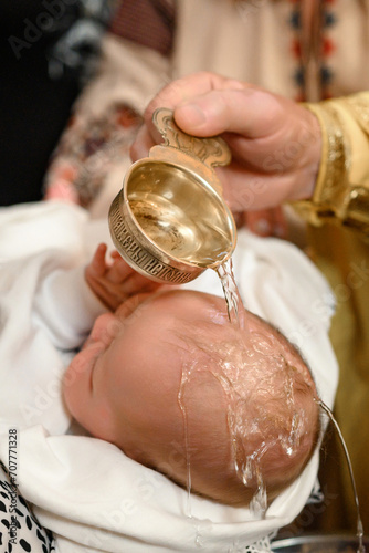 фотографія A priest pours water on the head of a small child during a Christian rite of baptism in a church