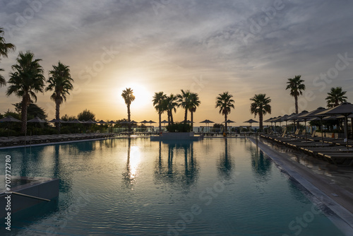 Sunrise over the pool and sunbeds. On the background of the sea coast. Big palm trees. © Roman Bjuty