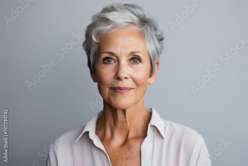Portrait of a smiling senior woman with grey hair looking at camera against grey background
