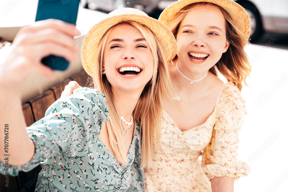 Two young beautiful smiling hipster female in trendy summer dresses  clothes. Blond carefree women posing in the street. Positive models having fun at sunny day. Going crazy. In sundress, take selfie
