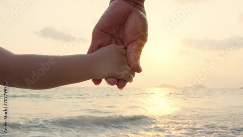 Close up Asian senior and little child boy holding hands on the beach with sunset on summer vacations together.