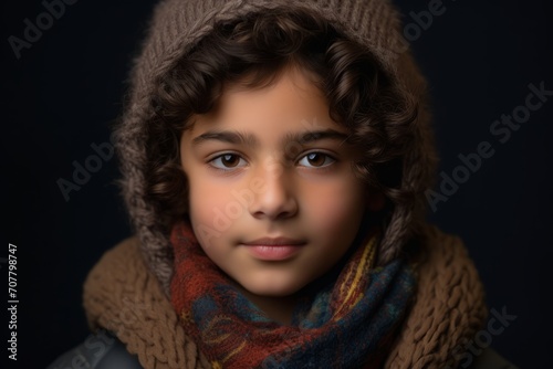 Portrait of a boy in a warm scarf and hat on a dark background.
