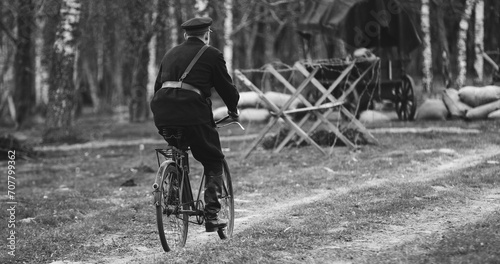 Re-enactor Dressed As Nkvd Forces Rides A Bike. Peoples Commissariat For Internal Affairs, Abbreviated Nkvd, Was Interior Ministry Of The Soviet Union. Black And White . photo