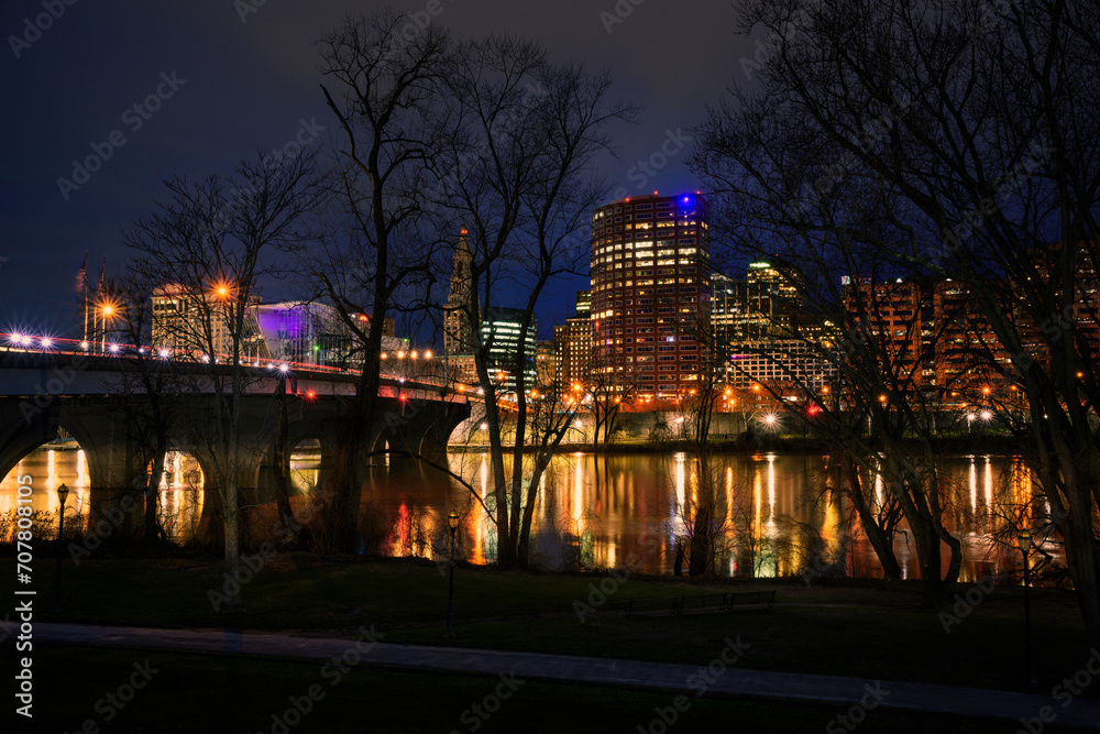 Hartford Skyline behind bare tree branches at night over the Connecticut River, USA