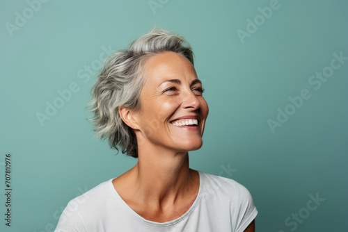 Close up portrait of beautiful middle aged woman with grey hair laughing and looking up over blue background