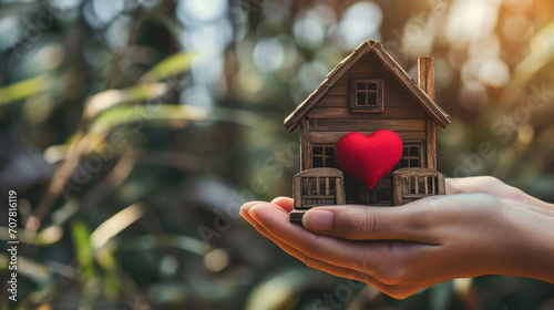 Home sweet home concept. Dream housing. Real estate. Hands holding miniature house with a red heart outdoors on a sunny summer day. photo
