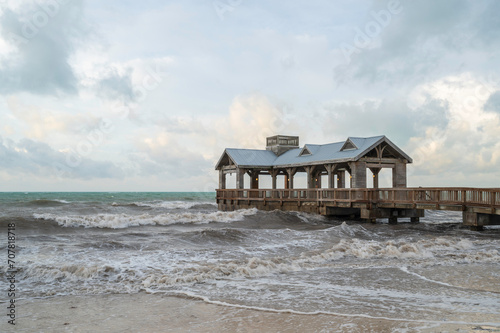 A wooden pier, with a covered portion at the end, reaching out into a choppy, rough sea © parkerspics