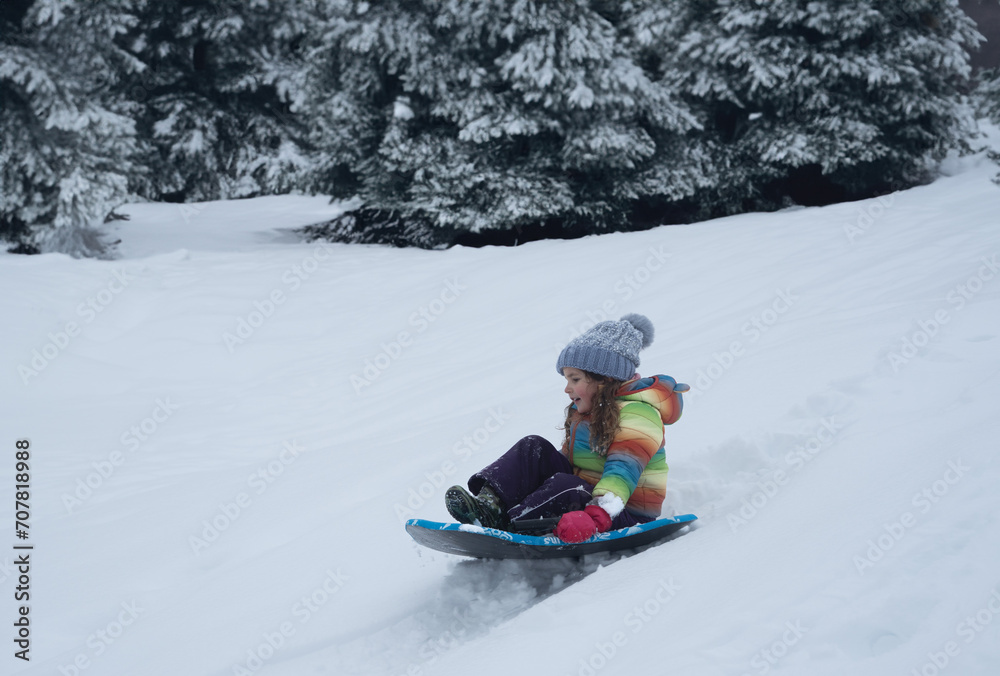 Little girl with rainbow jacket sledging down a snowy hill. High quality photo