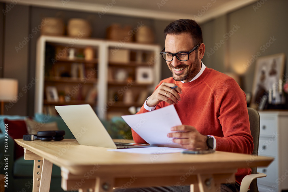 Ταπετσαρία A smiling male remote worker comparing a document in his hand to the one on his laptop