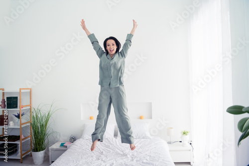 Photo portrait of attractive young woman jump bed raise hands cheerful dressed stylish gray pajama isolated on white modern interior design photo